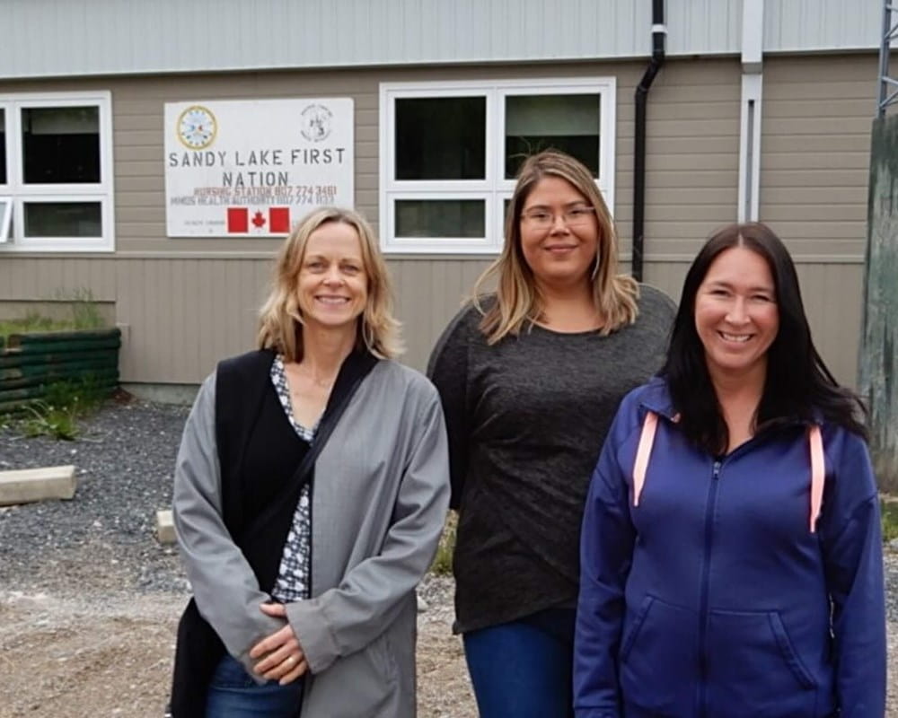 Dr. Samantha Wells, Krystine Abel and Dr. Renee Linklater outside the nursing station in Sandy Lake First Nation