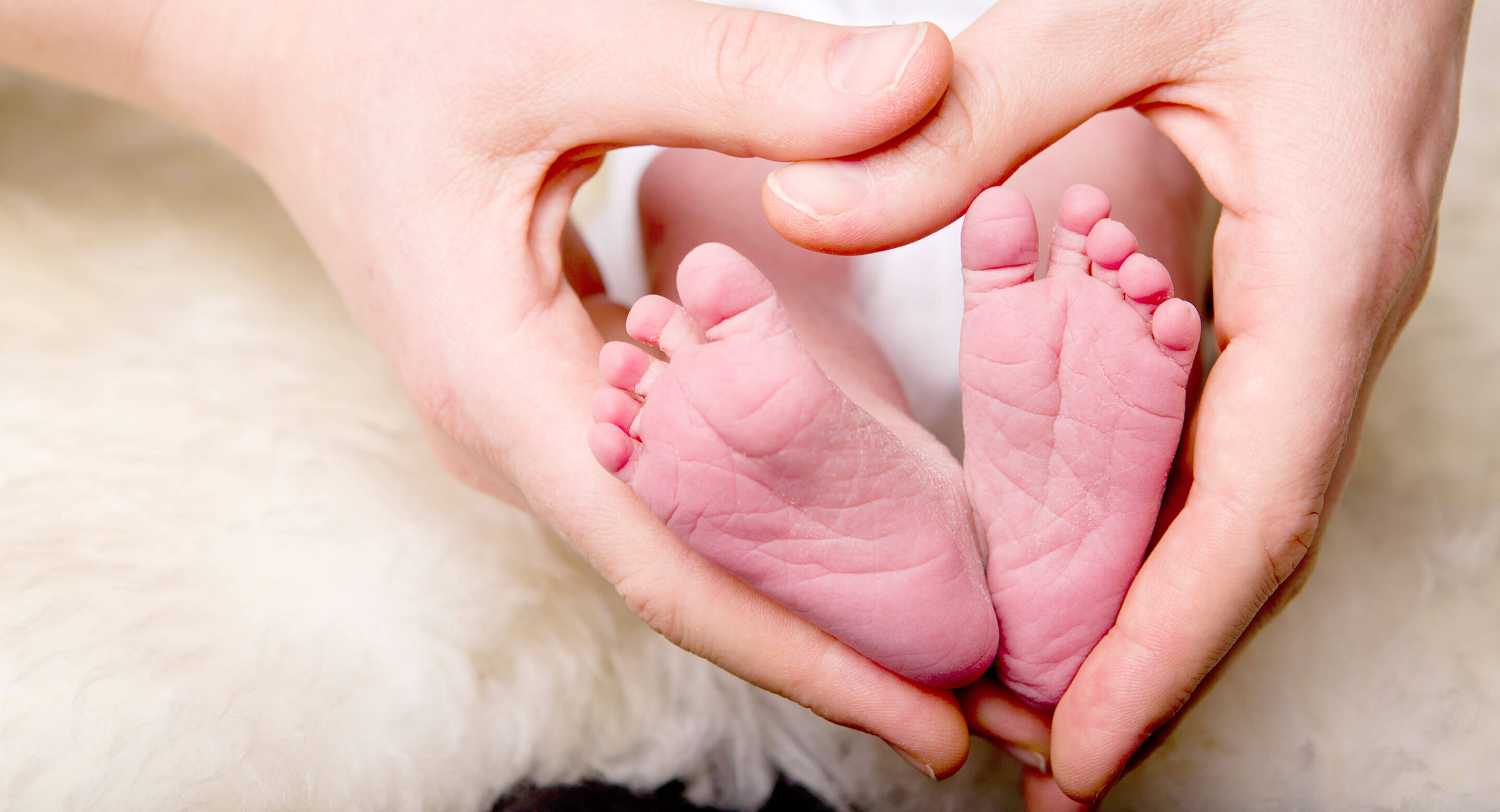 Adult hands form a heart around baby's feet.
