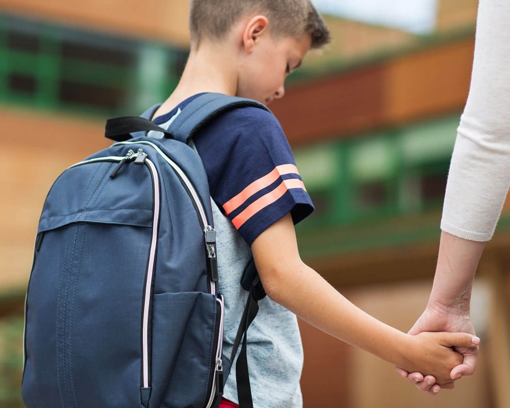 Sad boy reluctantly returning to school being lead by parent.
