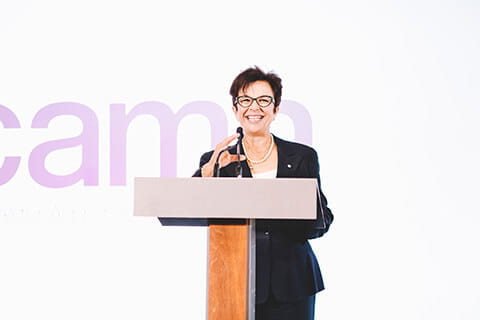 CEO, Catherina Zahn in a black blazer talking in front of a wooden podium. 