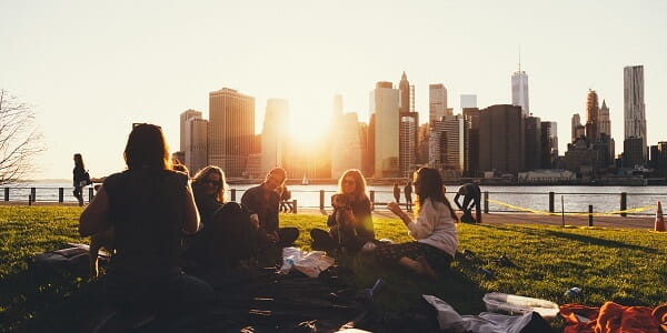 A group of women having a picnic in a park with the city line and sunset behind them. 