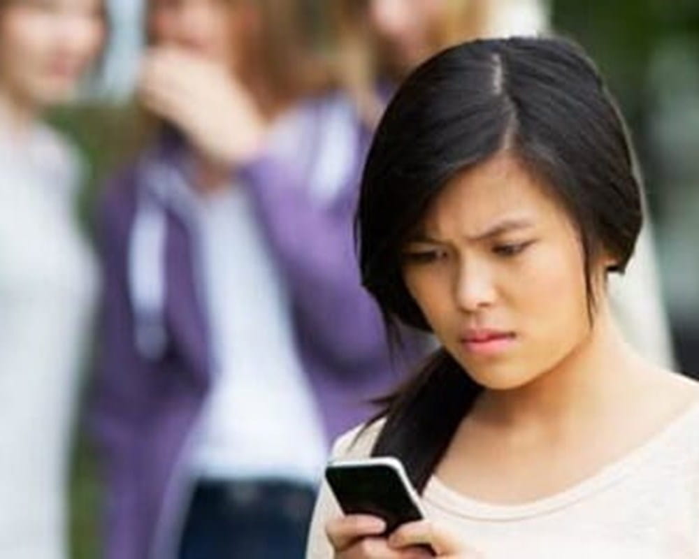 A young girl looking at her phone and is upset about something on the screen.