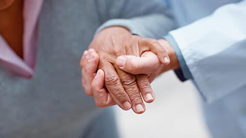A doctor's hand supporting an elderly person by holding onto the person's hand. 