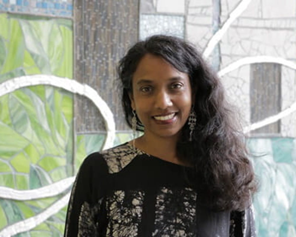 A woman of colour wearing a black and white blouse smiling.