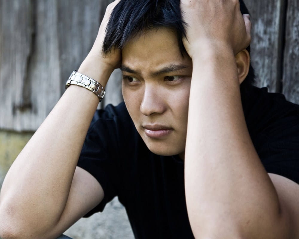 Young Asian man holding his head, looking sad.