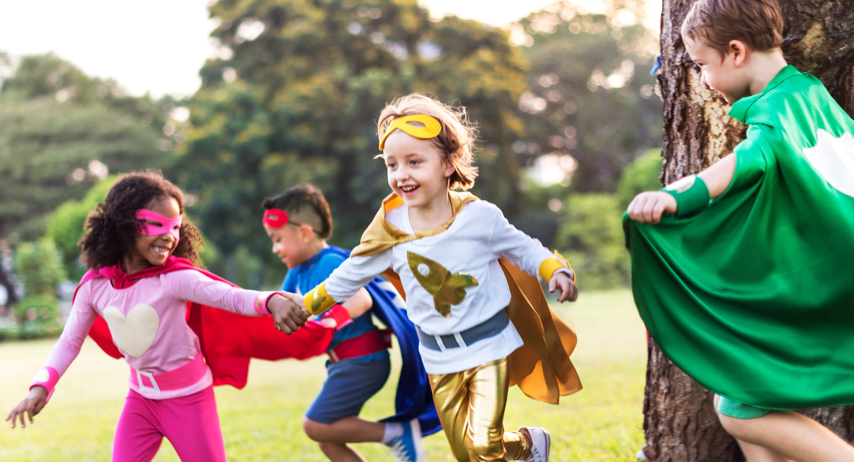 Kids dressed as superheroes playing in a field.