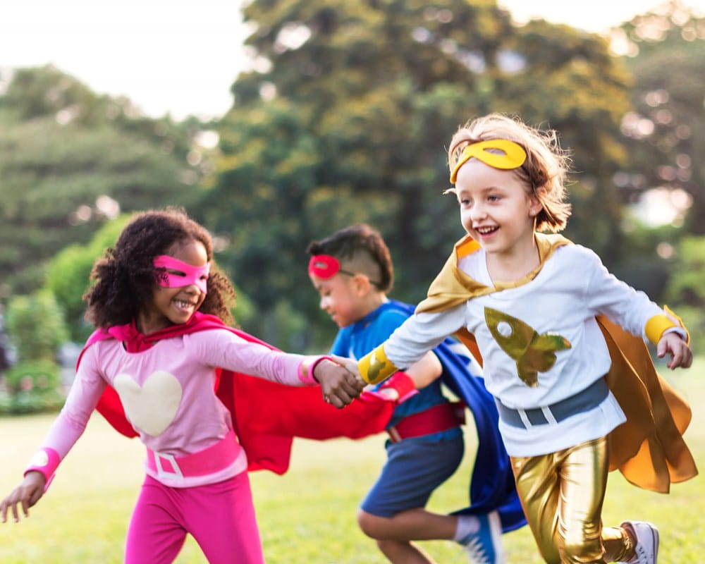 Kids dressed as superheroes playing in a field.