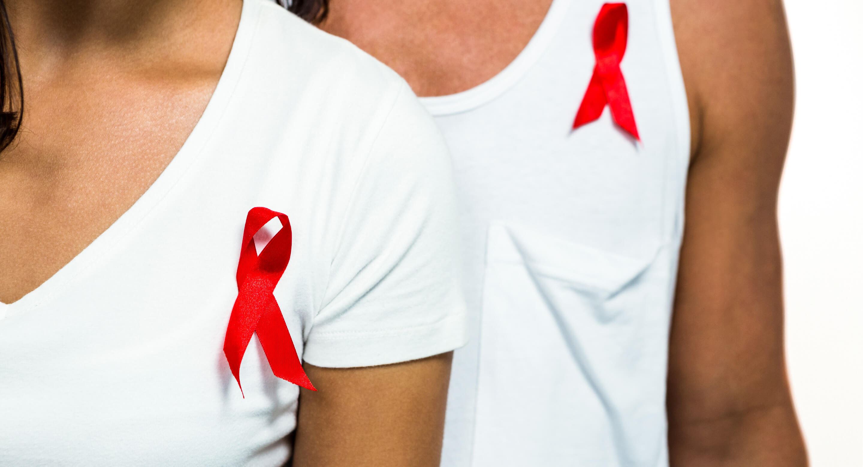 Close up image of two adults wearing red ribbons for AIDS awareness.