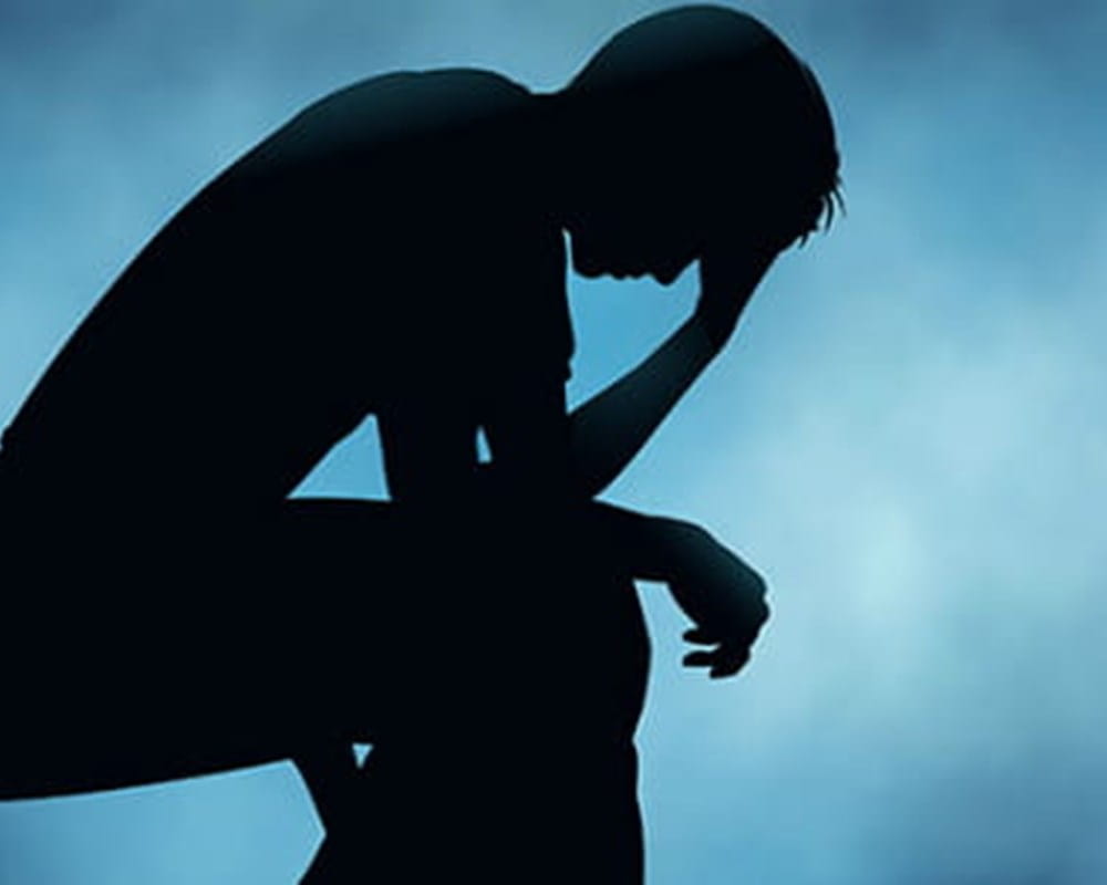A shadow of a person sitting on a bench looking upset with a blue background.