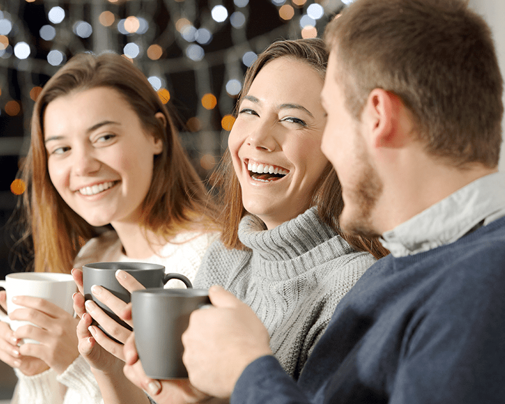 Three adults enjoying hot beverages in mugs against a festive background.