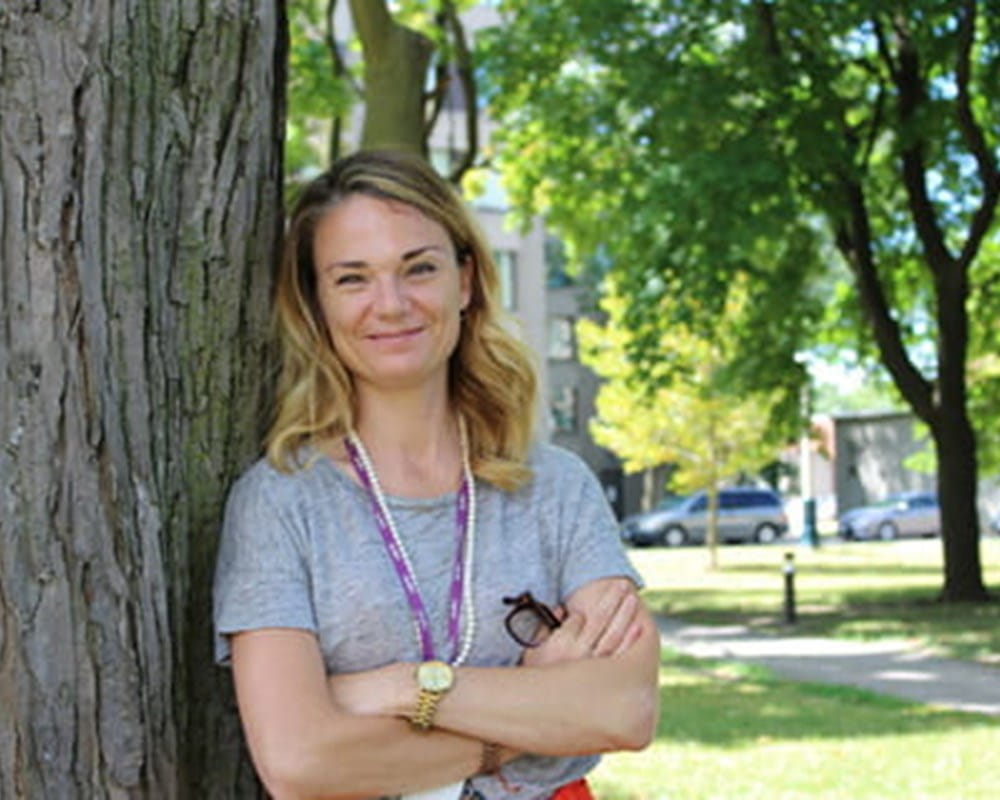 Susan Roman wearing a grey T-shirt and the purple CAMH lanyard leaning against a tree.