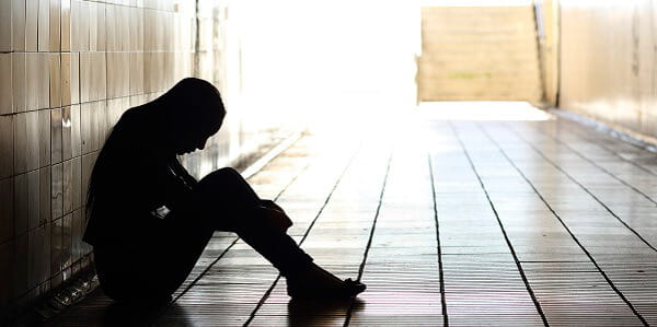 A woman sitting in a dark hallway looking down, upset. 