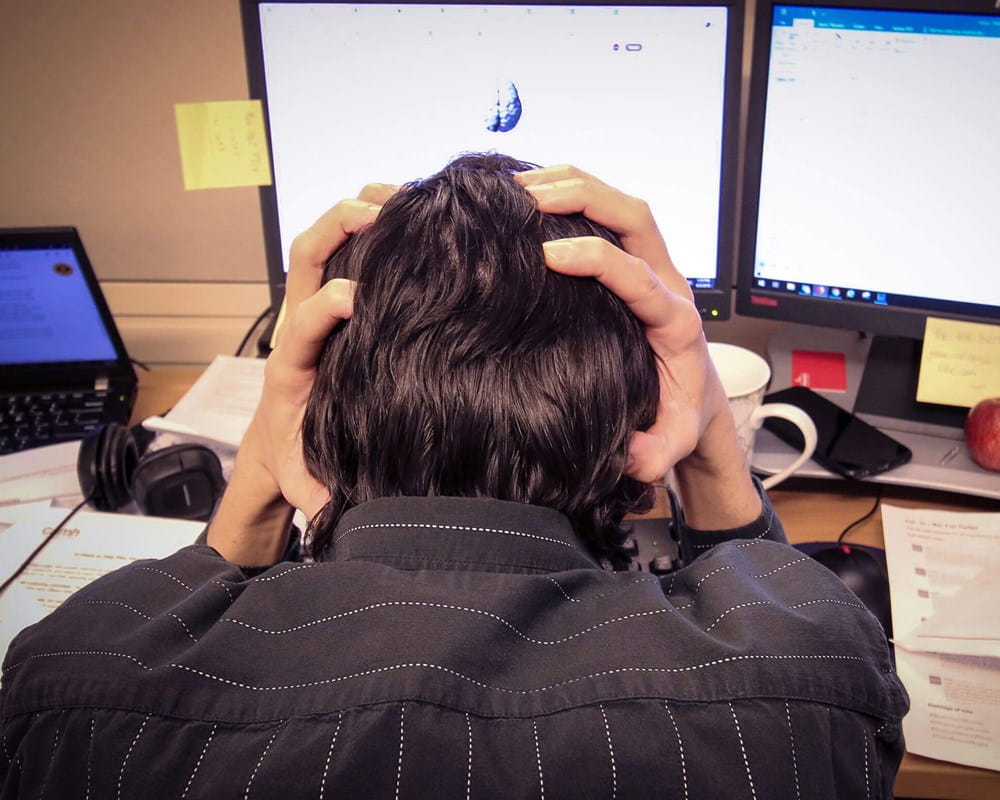 Man holding head in cluttered workspace