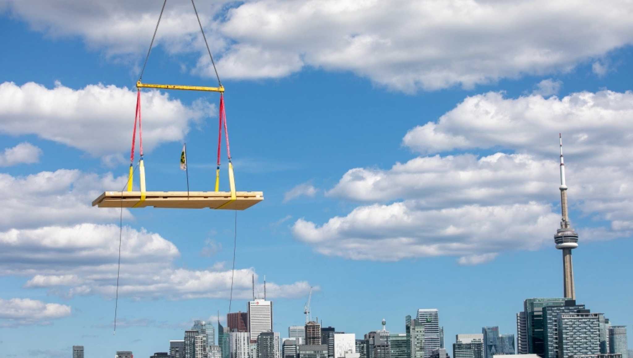 Image of lumber being lifted by a crane with the Toronto skyline in the background